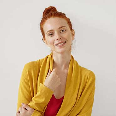 Adorable young female with ginger hair, freckles and shining eyes full of happiness, wearing yellow and red clothes, smiling gently into camera being glad to meet her friends or recieve message